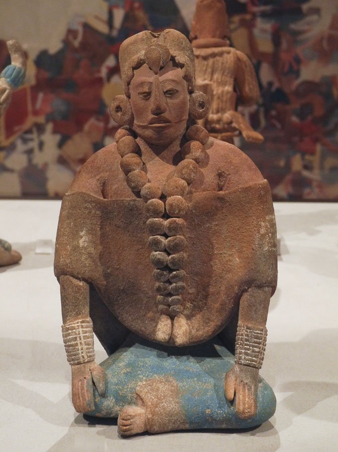 A seated Maya ceramic figure wearing a skirt adorned with Maya blue pigment showcasing vibrant coloration.